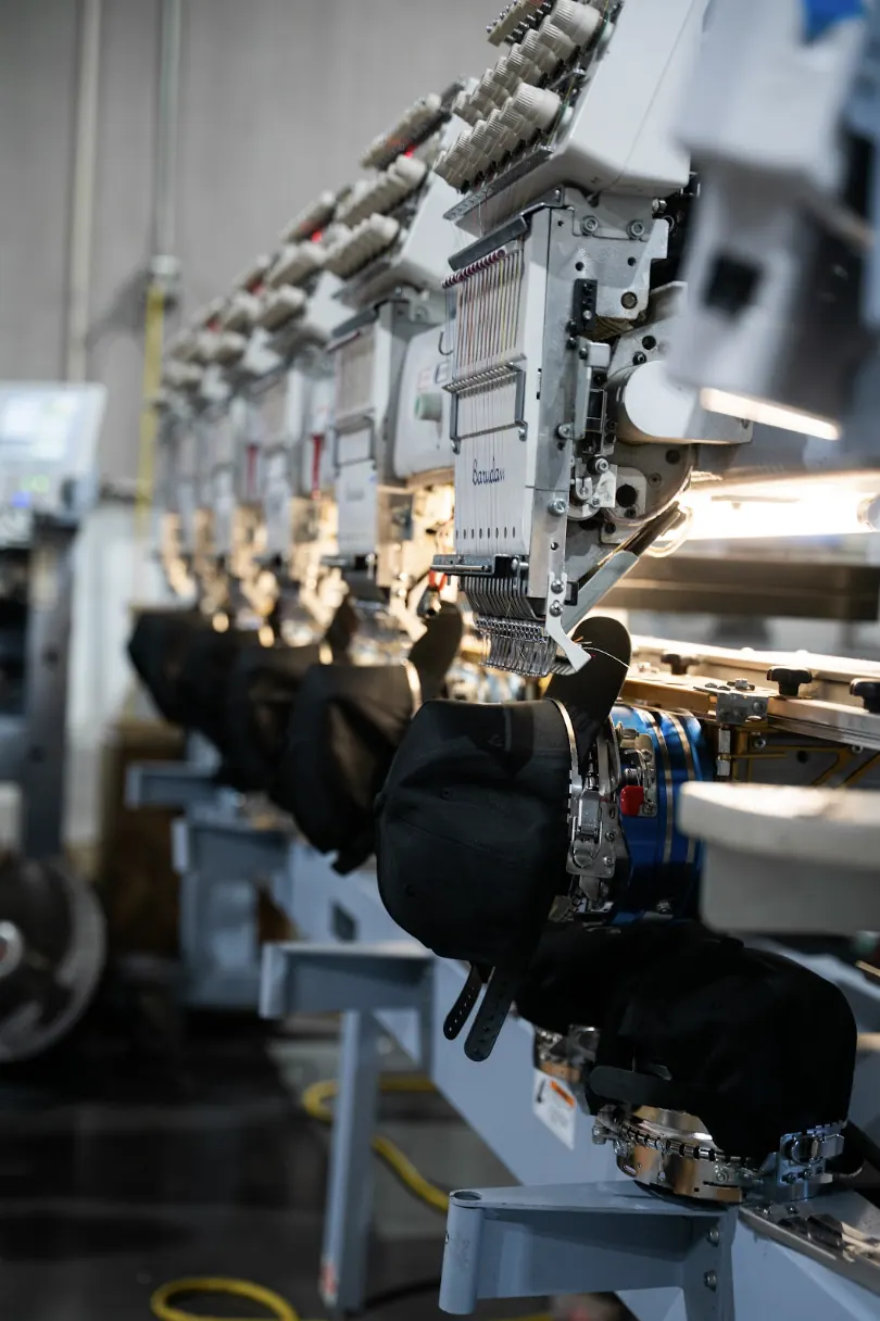 Row of cap driver attachments running custom snapback embroidery on Barudan multi-head machines