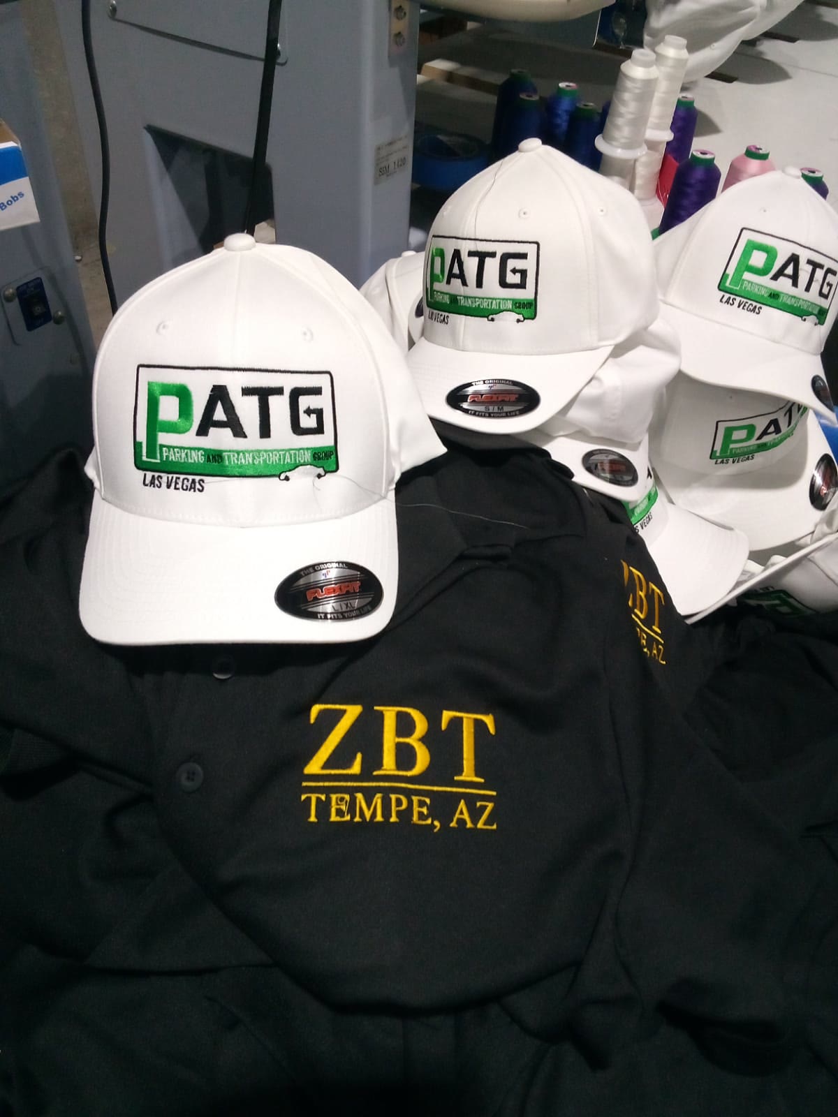 Dual-program run — green/black flex-fit caps + gold Greek-letter polos