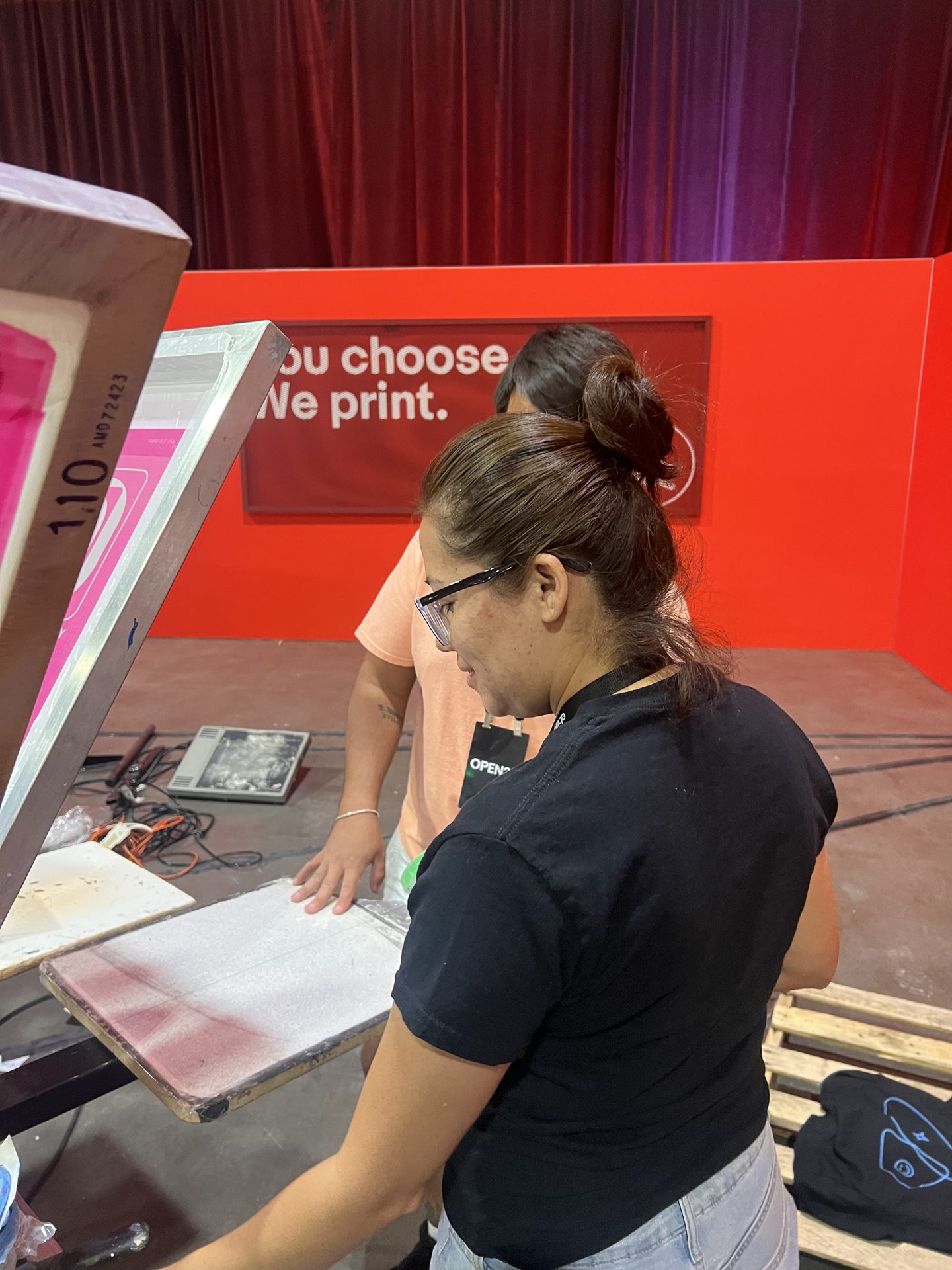 Live screen-printing operator pulling a pink ink print at a 'You choose. We print.' Vegas activation