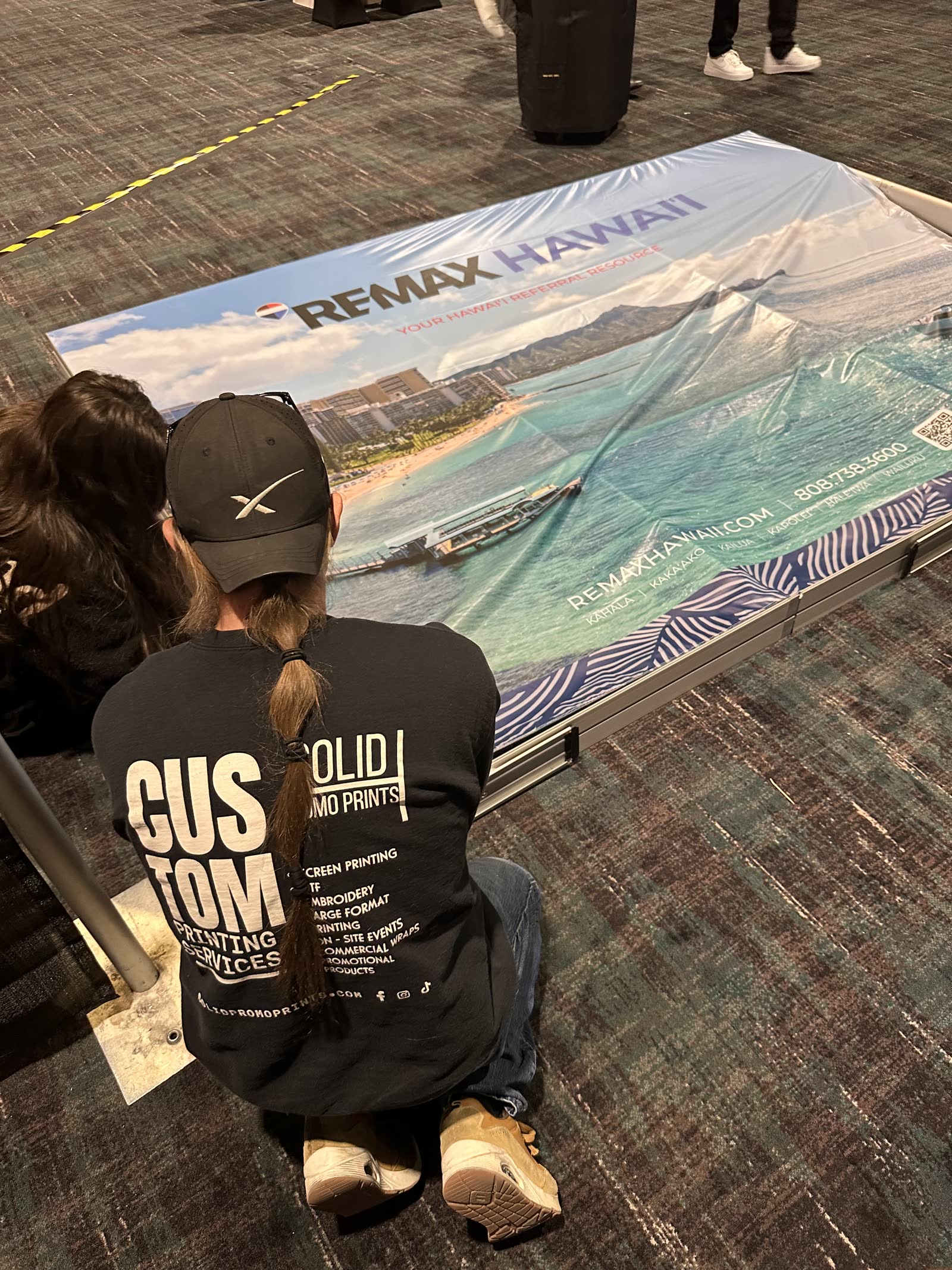 Solid Promo Prints crew loading a RE/MAX Hawaii SEG silicone-edge fabric graphic into a slim aluminum frame on the Las Vegas convention floor