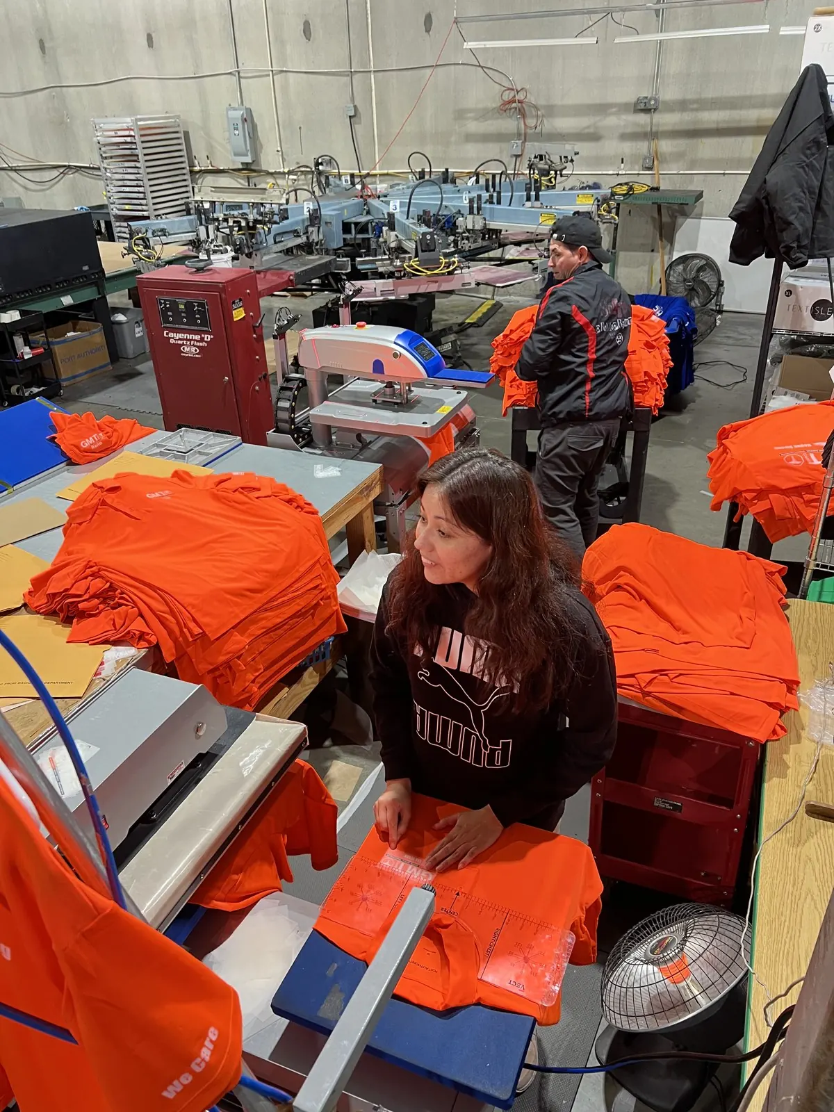 GMT Care Vegas Strong safety-orange staff shirts being folded and heat-pressed in the Solid Promo Prints production floor