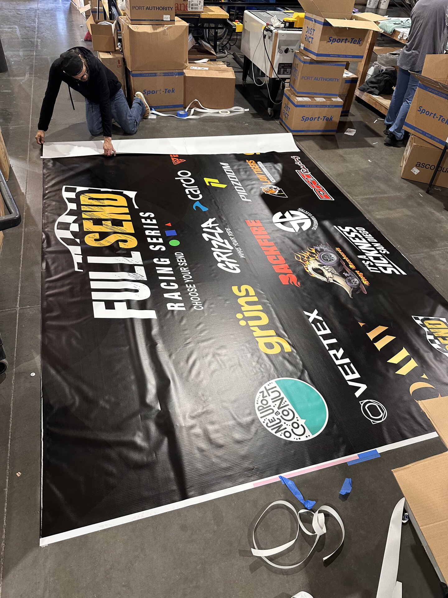 Large 13 oz vinyl banner laid out on the Solid Promo Prints production floor during finishing, showing full-color sponsor logos for a racing event